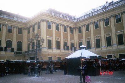 Neoclassical courtyard with light beige façade, arched windows, and decorative cornices. Snow-covered market stalls line the ...