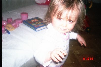 Vintage indoor portrait of a young child (approx. 2-3 years) seated at a table with 1990s-era toys: pink plastic cups, a toy ...