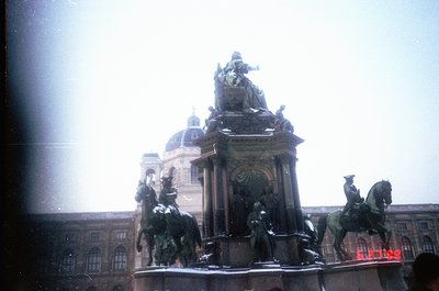 Vintage equestrian monument with four horsemen flanking a central pedestal, set against a grand neoclassical building with do...