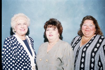 Three women pose formally in 1980s/90s attire—polka-dot blazer, cream blouse with buttons, and striped sweater with pearl nec...