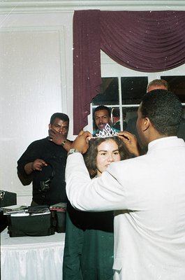 A young girl in a white top has a tiara placed on her head by a man in a white shirt, likely at a 1990s-2000s birthday party....