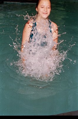 Young girl mid-dive in an indoor pool, creating a splash. Wearing a blue one-piece swimsuit with a textured pattern. Likely m...