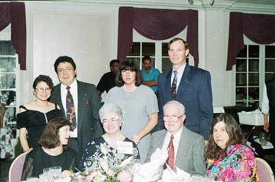 Family portrait at a formal indoor event, likely a wedding or anniversary, featuring seven adults seated and standing around ...
