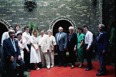 Group portrait in a grand brick courtyard with arched entryway, 1970s. Formal attire—men in suits, women in dresses—suggests ...