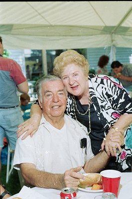 Couple sharing an affectionate moment at an outdoor event, likely mid-1990s. Man in white polo, woman in black-and-white patt...
