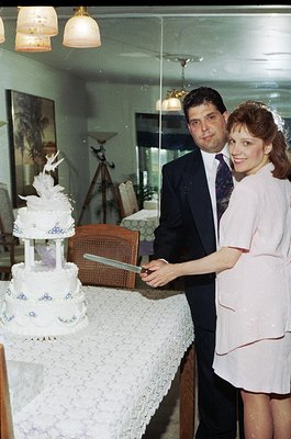 Vintage wedding cake cutting scene in a classic indoor setting, featuring a three-tiered cake with floral blue accents. The g...