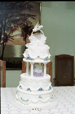 Elegant three-tiered wedding cake with vintage floral motifs, featuring a bird figurine atop. Decorated in white with blue ac...