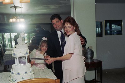 Family wedding celebration with three generations: bride (white lace gown), groom (dark suit), and young girl (dress with rib...