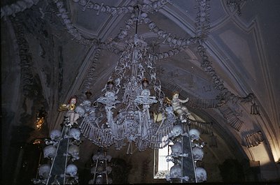Baroque-style chandelier adorned with cherubic figures and ornate crystal clusters, suspended in a vaulted ceiling. Likely Eu...