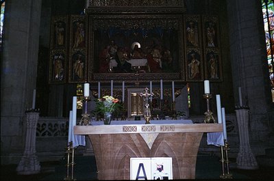 Gothic-style altar with ornate wooden carvings and central crucifix, flanked by candle holders and floral arrangements. Stain...