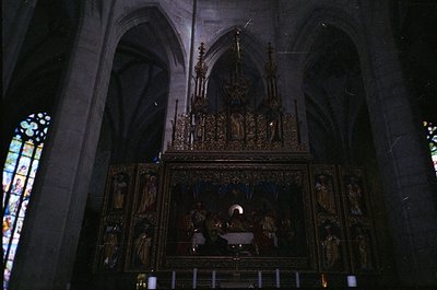 Gothic-style altar with ornate wooden carvings depicting religious scenes, flanked by stained-glass windows. Intricate detail...