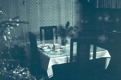 Vintage monochrome dining scene featuring a round glass-topped table set with tiered cake, floral centerpiece, and vintage ch...