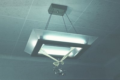 Minimalist industrial pendant light with rectangular fluorescent tube and geometric metal frame suspended from rough concrete...