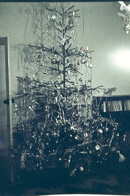 Vintage Christmas tree adorned with metallic ornaments, tinsel, and a single red star topper in a modest indoor setting, like...