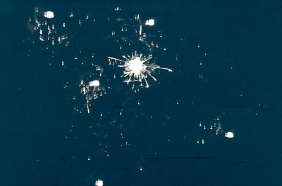 Close-up of shattered glass fragments on a dark surface, likely from a broken window. Radial cracks radiate from a central im...