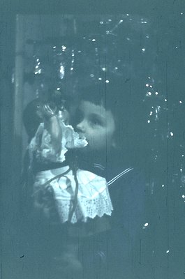 Vintage sepia-toned photo of a child in early 20th-century attire, holding a small object (likely a toy or tool) near their m...