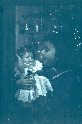 Vintage sepia-toned reflection of a woman holding a child in a patterned dress, captured through a frosted glass window. The ...