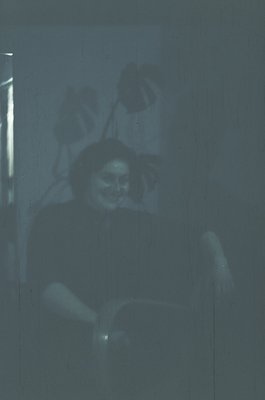 Vintage monochrome portrait of a seated individual in dim lighting, likely from the 1950s–1970s. The person holds a book or o...