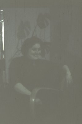 Vintage projection of a blurred silhouette of a seated person against a light source, likely from a slide or film. The figure...