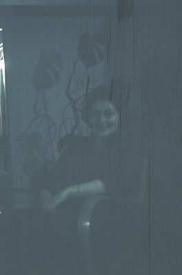 Silhouetted figure seated on a window ledge, back to camera, framed by a frosted glass pane. Urban setting with faint streetl...