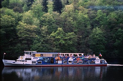 Passenger ferry "PPS" navigating a forested river, likely in Norway’s fjords. Mid-20th century design with open-air seating a...