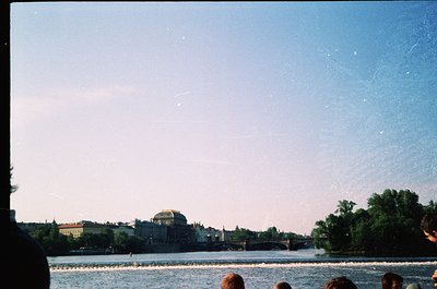 Vintage shot of a riverbank scene with a distant bridge and domed building, likely Warsaw’s Palace of Culture. Soft focus and...