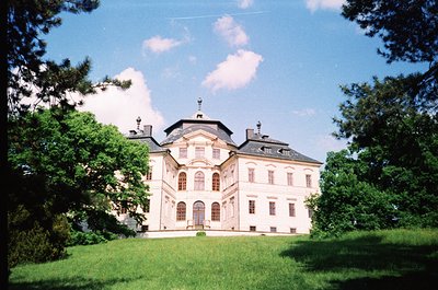 Neoclassical mansion with symmetrical façade, central pediment, and mansard roof. Lush green lawn and mature trees frame the ...