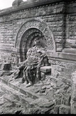 Monolithic stone relief sculpture of a seated figure draped in flowing robes, integrated into a stone archway with intricate ...