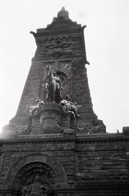 Monumental equestrian statue atop a stone tower, likely 19th-century European. Central figure on horseback flanked by kneelin...