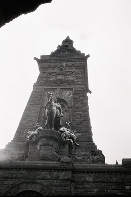 Neoclassical stone monument featuring a central equestrian statue atop a grand pedestal, flanked by smaller figures. Intricat...