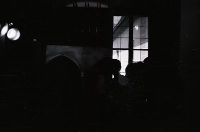 Silhouette of a person standing near a window with grid-patterned glass, illuminated from behind by artificial light. Reflect...