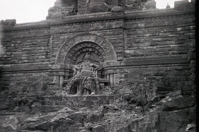 Relief sculpture on weathered stone wall, featuring intricate carvings of seated figures in dynamic poses. Likely part of an ...