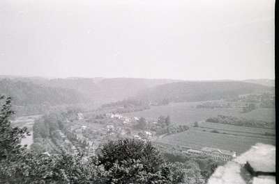 Vintage black-and-white aerial view of a rural valley with winding roads, clustered buildings, and agricultural fields. Dense...