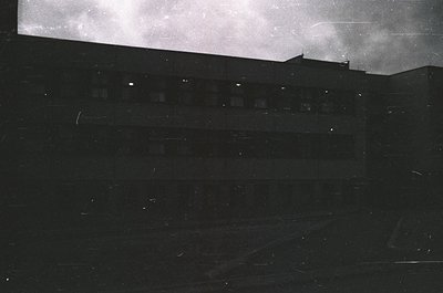 High-contrast black-and-white shot of a multi-story building’s rooftop edge, likely from a low-angle perspective. Horizontal ...