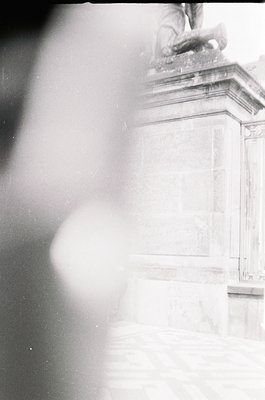 Blurred black-and-white close-up of a classical stone monument featuring a seated figure with wings, likely a cherub or angel...