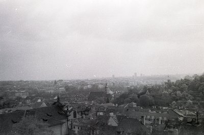 Vintage aerial view of a European cityscape with dense, low-rise architecture and a prominent church spire. Fog obscures dist...