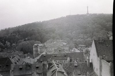 Vintage black-and-white aerial view of a European hillside town with dense, sloped rooftops and a prominent hilltop tower. Ar...
