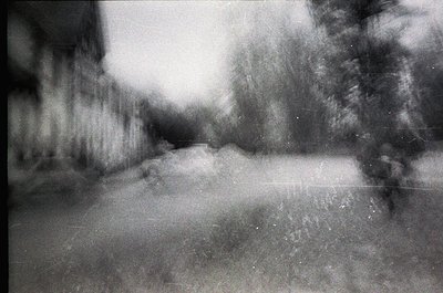 Vintage monochrome street scene with soft focus, likely 1960s–1980s. Blurred urban alleyway flanked by indistinct buildings a...