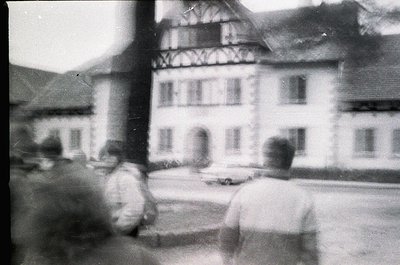 Vintage black-and-white shot of a European village square featuring timber-framed half-timbered architecture. Three blurred f...