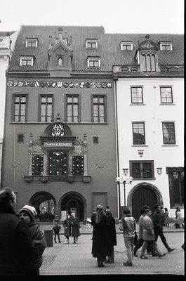 Historic European town hall façade with Gothic Revival details, including ornate crest and arched entrance. Crowd of mid-20th...
