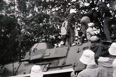 Vintage black-and-white photo of a Soviet T-34 tank with soldiers atop, likely mid-1940s Eastern Front. Crowd in white caps (...