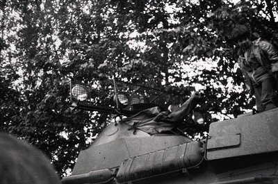 Vintage black-and-white photo of a Soviet T-34/85 tank crewman leaning over turret edge in dense forest, mid-20th century. Vi...