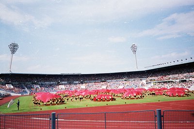 Vintage stadium scene featuring synchronized team in red uniforms and matching scarves forming a large logo on the field. Emp...