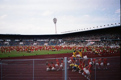 Massive stadium scene featuring synchronized cheerleaders in red and white uniforms performing on the field. Crowd fills tier...