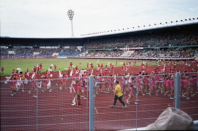 Vibrant stadium scene with mass fan celebration, likely a European football match. Crowds in red scarves and jerseys flood th...