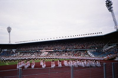 Large stadium crowd with choreographed dance performance on field, featuring uniformed dancers in white and red. Stadium seat...