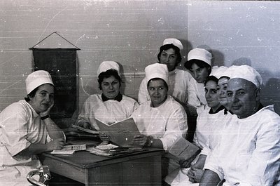 Black-and-white group portrait of medical staff in 1960s-70s uniforms—nurses in caps and white gowns, a male doctor in lab co...