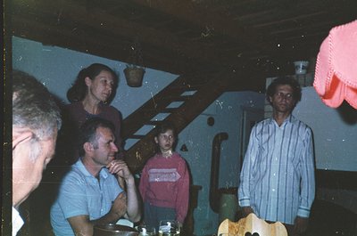 Vintage indoor gathering, likely 1980s–1990s, featuring five adults in casual attire—men in button-down shirts, women in swea...
