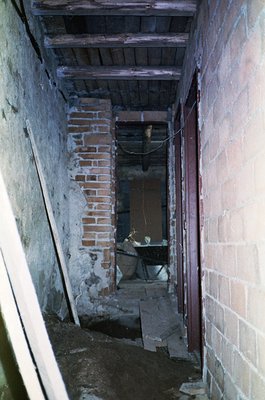 A dimly lit, narrow hallway showcasing aged brickwork and exposed wooden beams, likely from a historic residential or industr...
