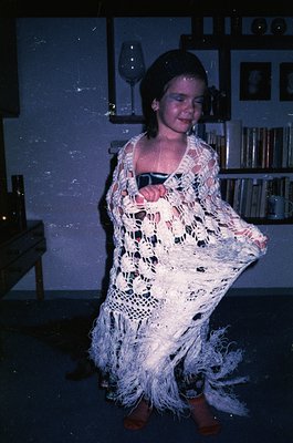 Vintage indoor portrait of a person in a crocheted flamenco-style dress with fringe, holding a wineglass. Bookshelves and fra...